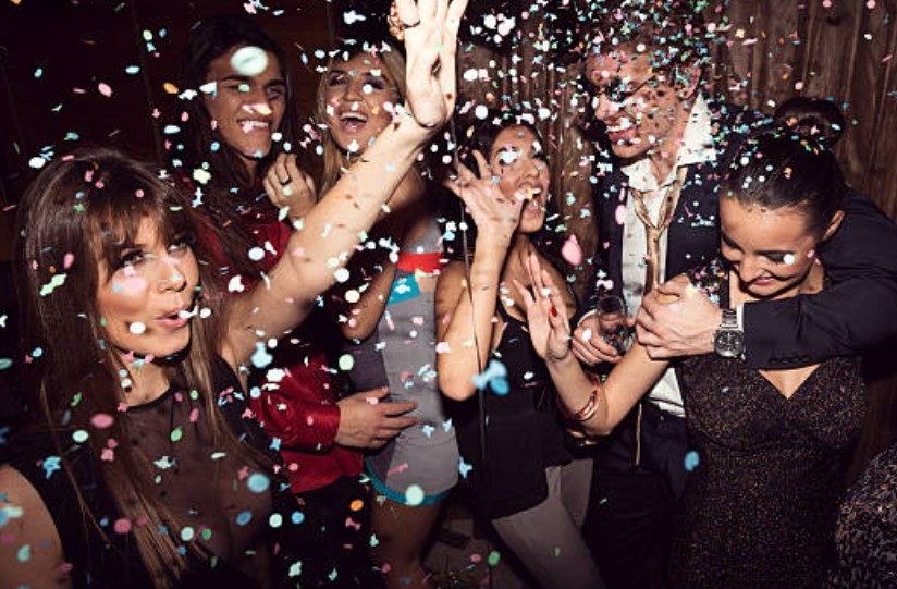 Six personnes rient et trinquent sous une pluie de confettis